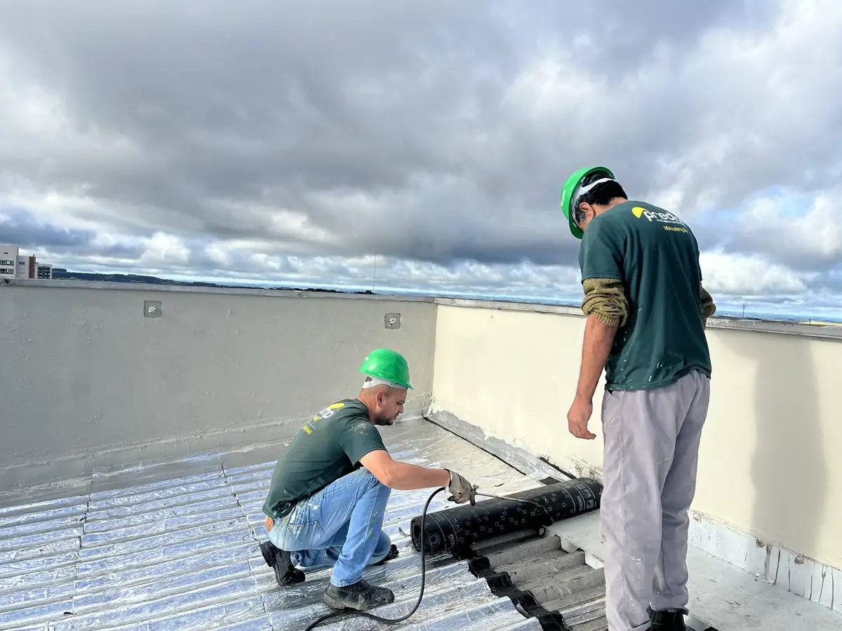 Colaboradores do Grupo Predial com capacete aplicando manta asfáltica com maçarico na cobertura de um edifício