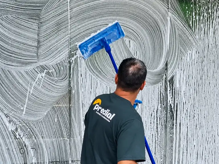Colaborador do Grupo Predial limpando a fachada de vidro de um edifício com a marca Predial visível