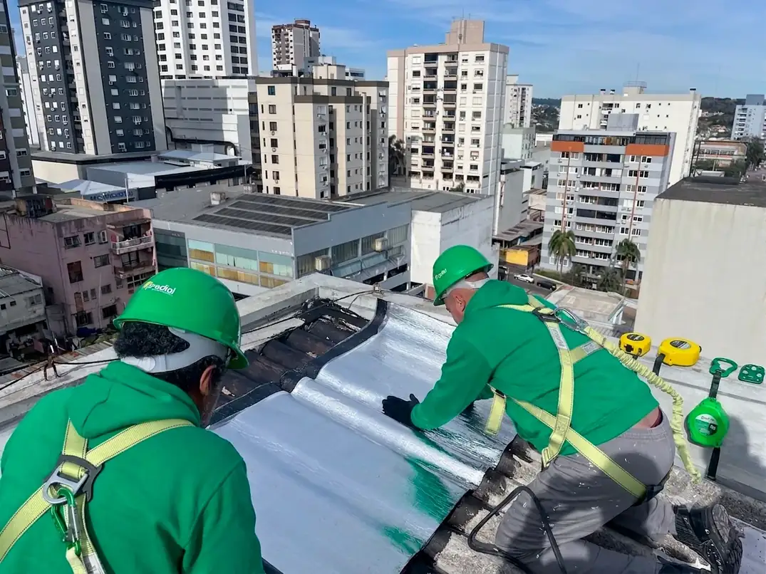 Trabalhadores do Grupo Predial com capacete e cinturão de segurança executando serviço em cobertura predial
