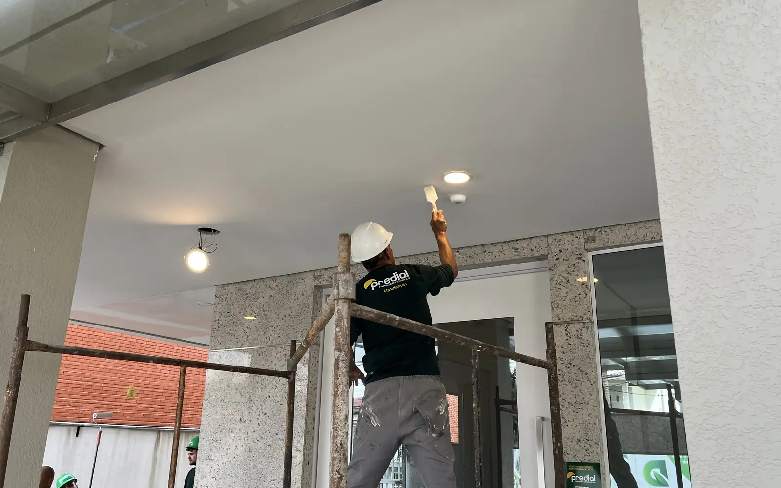 Pintor do Grupo Predial em andaime pintando o forro da área externa de um edifício
