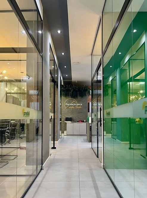 Corredor corporativo do Grupo Predial 360 com salas de vidro, parede verde e recepção ao fundo
